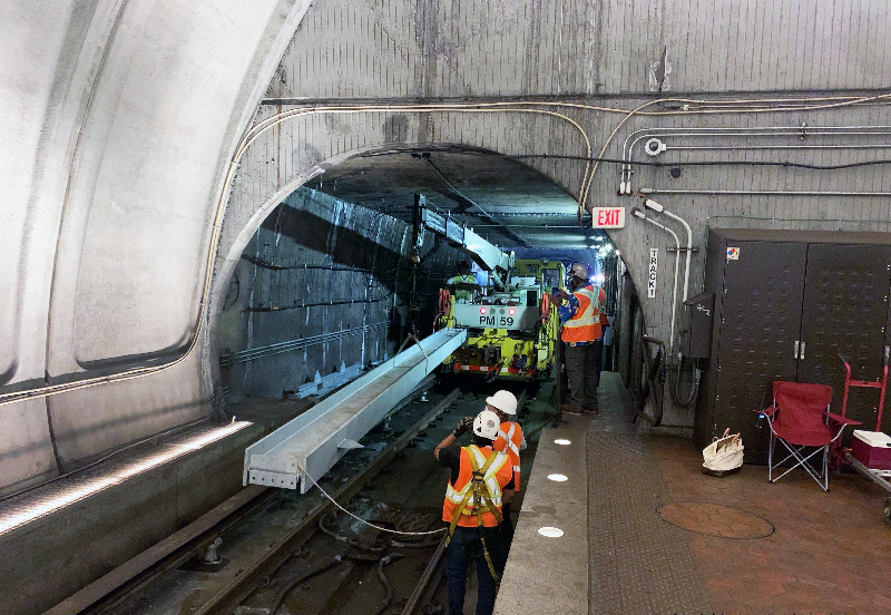 Due to the significant space limitations in the tunnel, and the longer length of the steel beams, special handling was necessary. Here, workers use the station platform for proper alignment before rolling down the tracks and setting the steel beams.