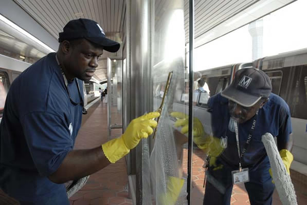 Metro employees clean a glass panel on a Metrorail station platform.