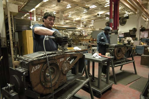 Employees work on repairing parts at a bus maintenance shop.